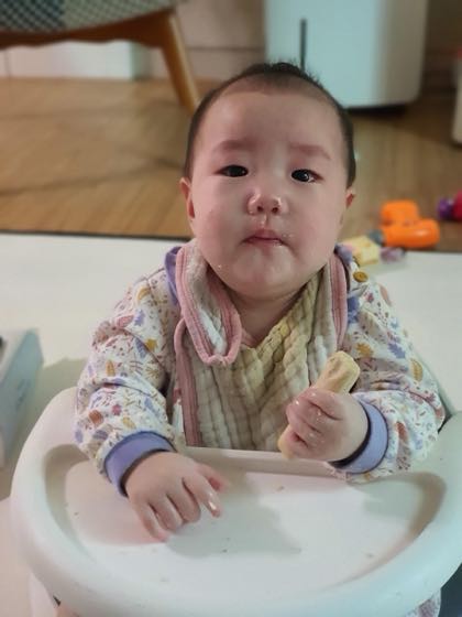 ハイチェアに座り手に持ったおやつを食べる赤ちゃん