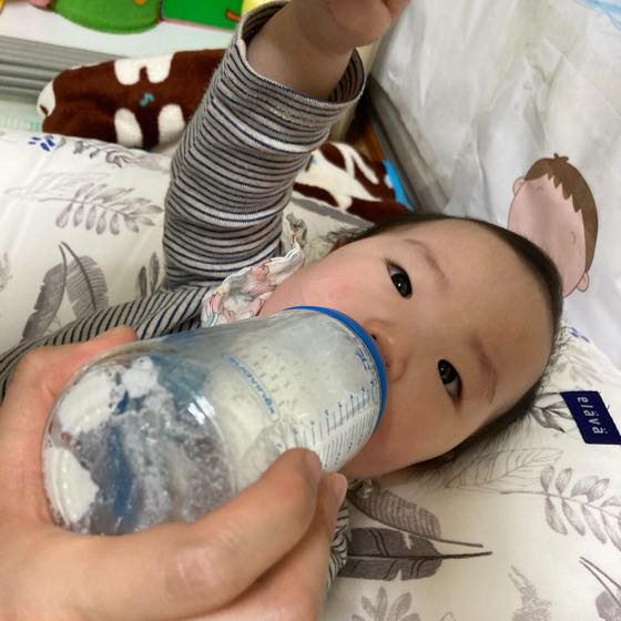 An adult feeding a baby fluids from a bottle