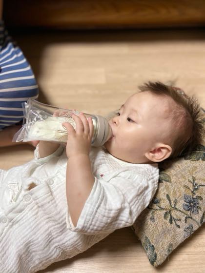 A baby lying down drinking breast milk from a bottle with a storage pack attached