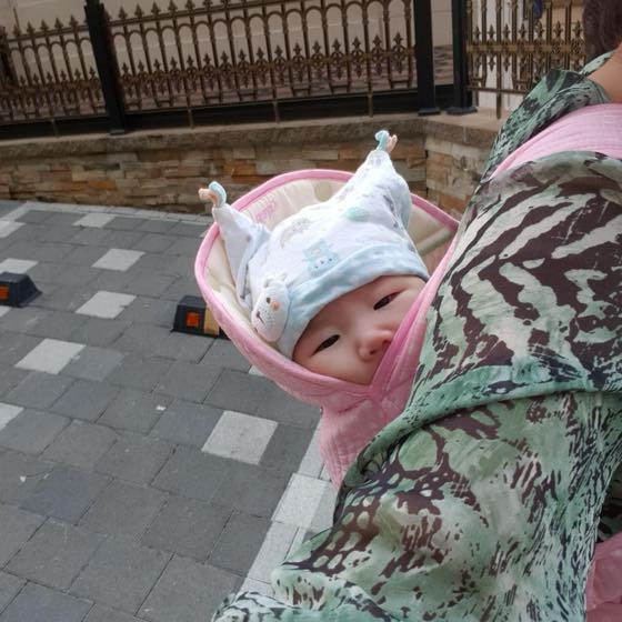 長袖の服と帽子を身につけ、抱っこひもで外出する赤ちゃん