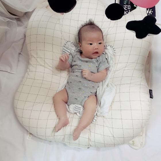 A baby lying on a cushion, moving its arms and legs freely as it plays