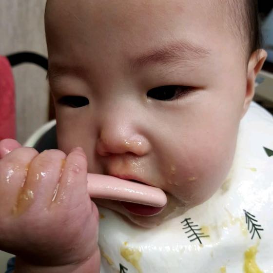ベビーチェアに座りスプーンで離乳食を食べさせてもらっている赤ちゃん