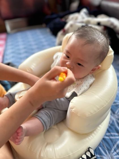背もたれのあるベビーチェアで支えられて座り、上半身と頭を立てている赤ちゃん