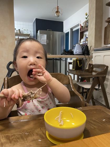 食卓で器を前に、自分で食べ物をつまんで食べる1歳過ぎの赤ちゃん