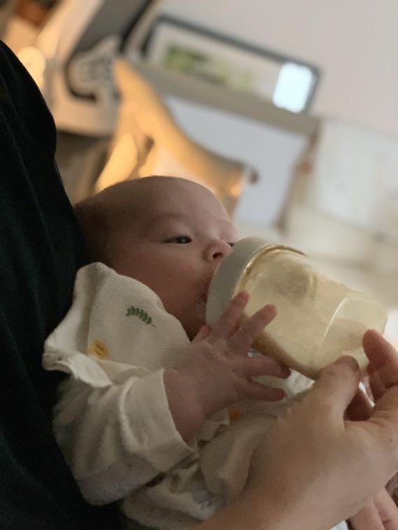 親の腕に抱かれて哺乳瓶でミルクを飲む赤ちゃん
