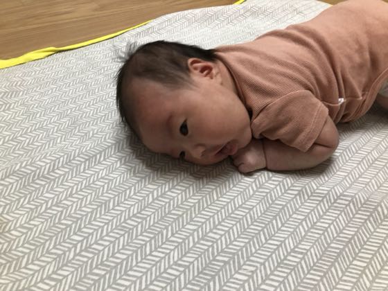 床のマットにうつ伏せで寝そべる新生児（タミータイム）