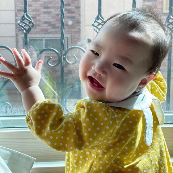 A smiling baby waving by the window