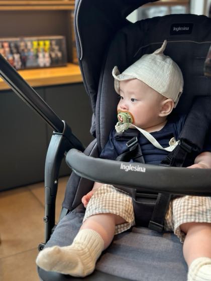 A baby in a brimmed summer hat and light shorts sitting in a stroller