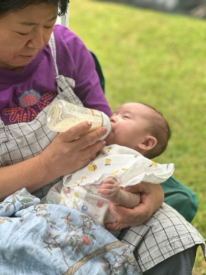 夏の外出中、日かげで赤ちゃんに哺乳びんで水分をあげる様子